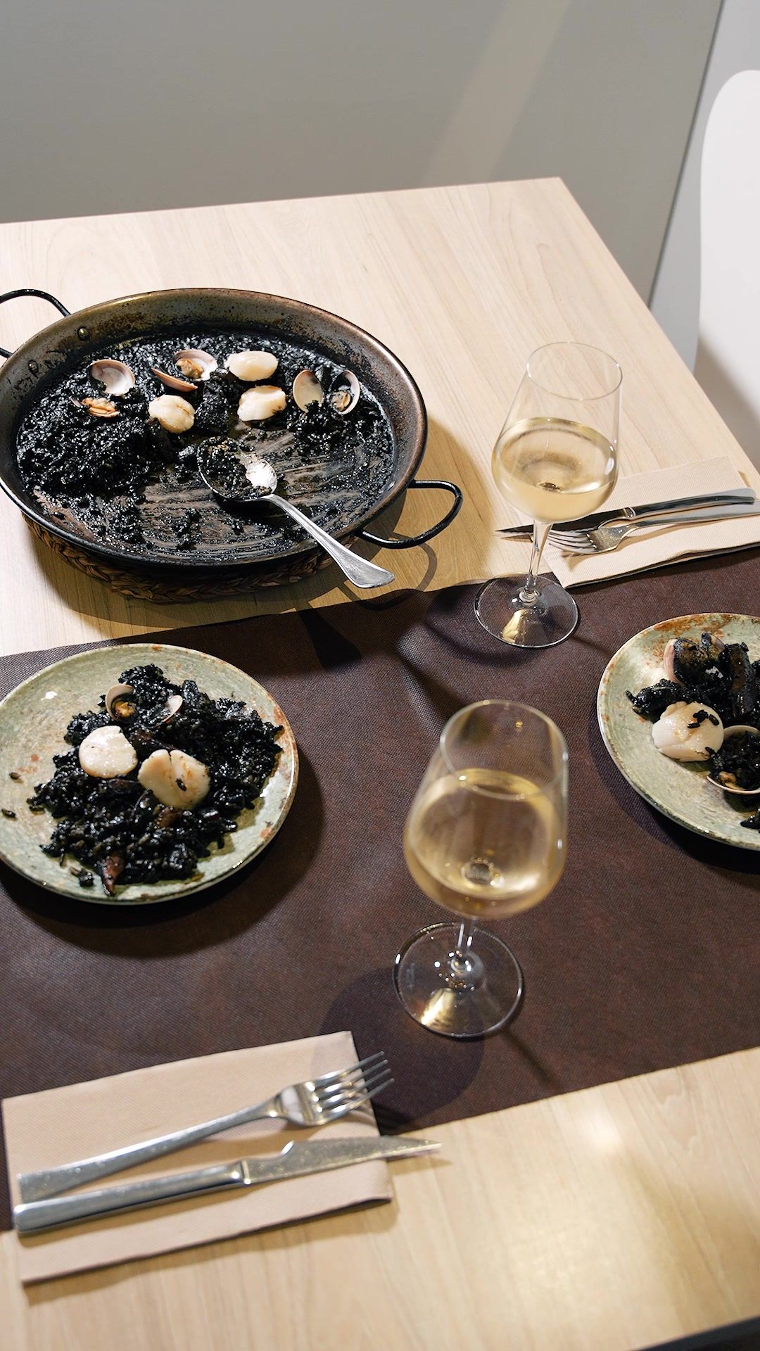 Paella d’arròs negre a taula amb plats servits i vi blanc