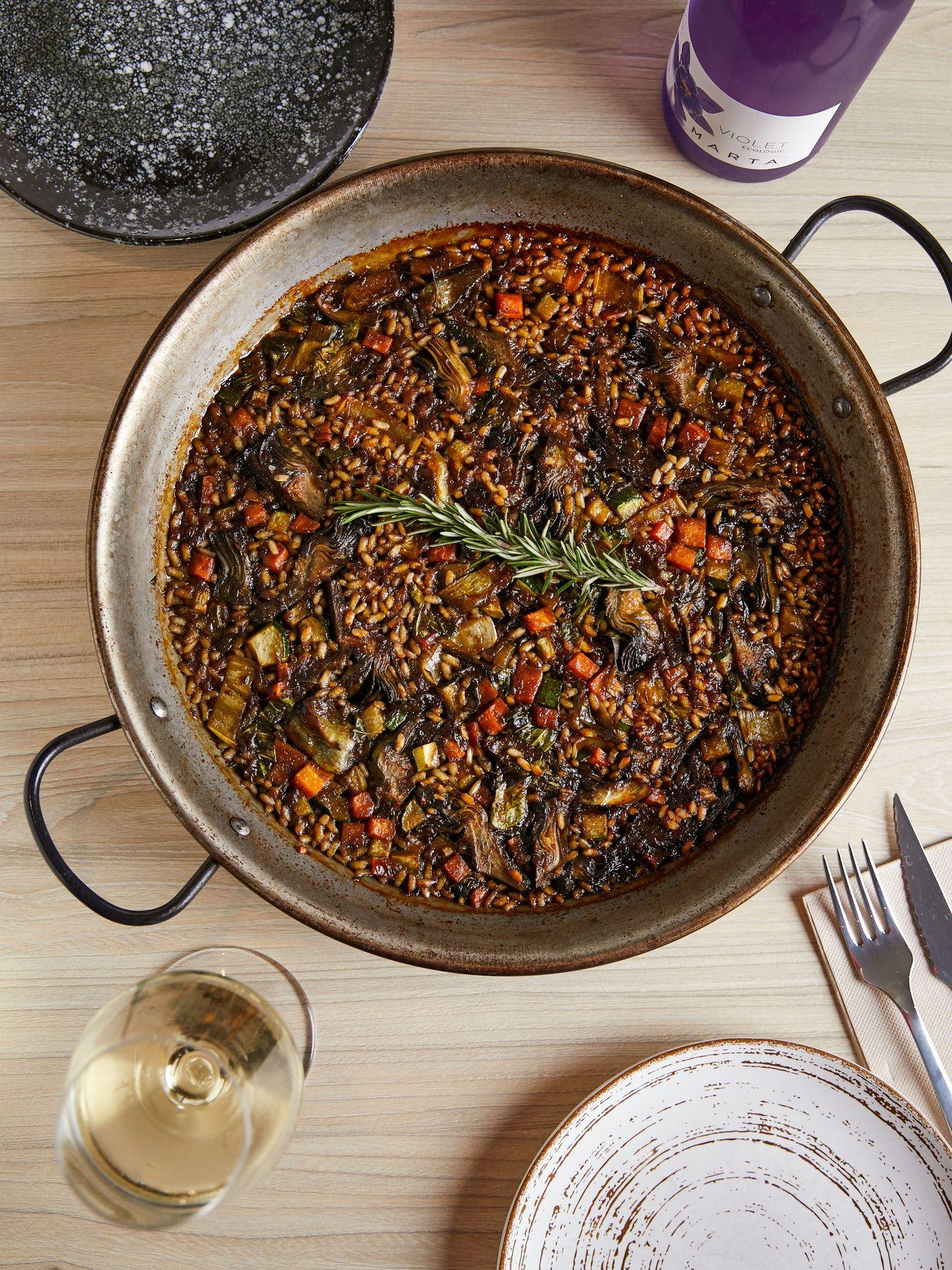 Paella de arroz de verduras en el centro de la mesa, con platos y copas de vino blanco